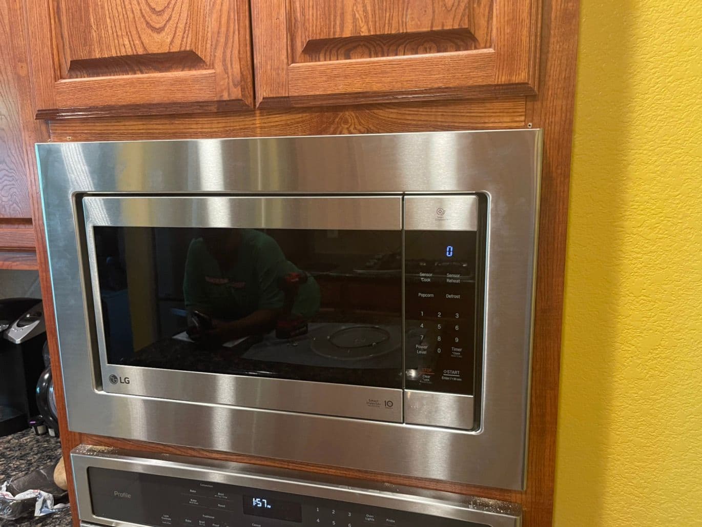 Stainless LG over-the-range microwave mounted under oak cabinets in a yellow kitchen