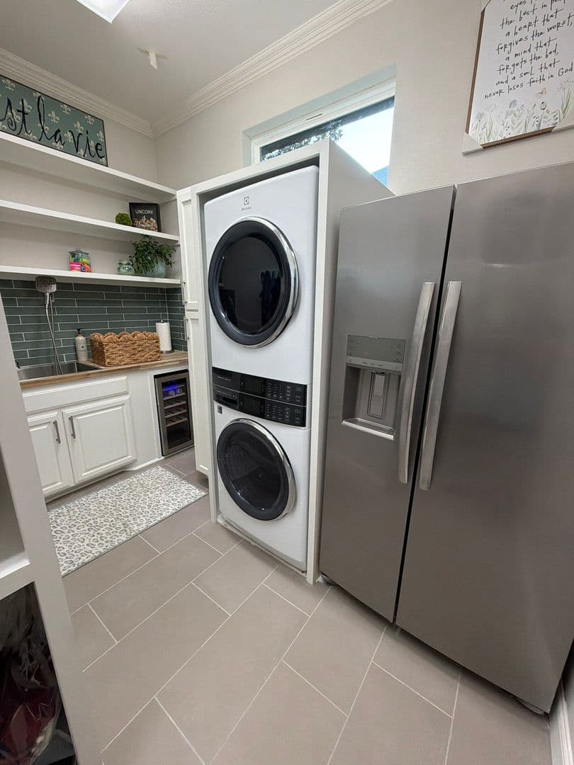 Newly installed stacked washer and dryer in a laundry room beside a stainless refrigerator