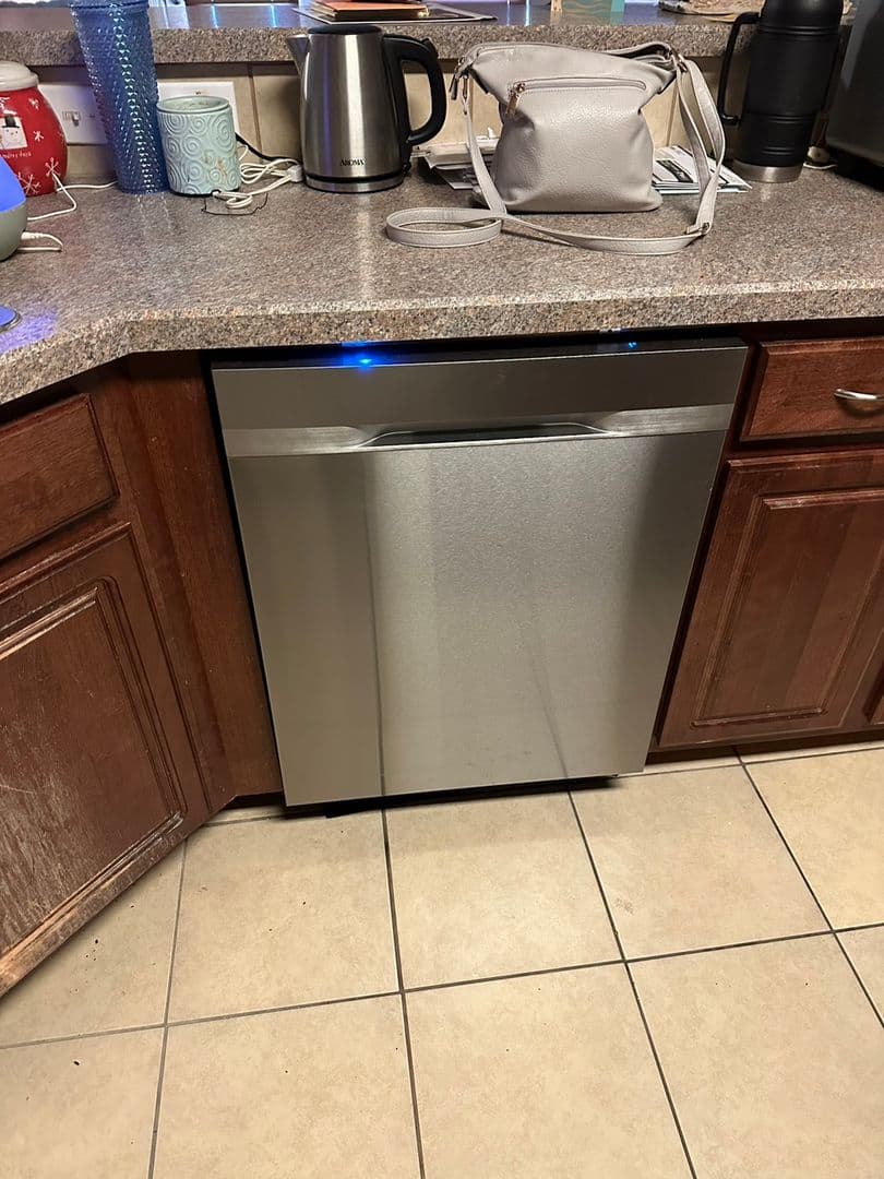 Stainless dishwasher installed under a granite countertop between cherry cabinets